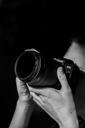 grayscale photo of person holding nikon dslr camera