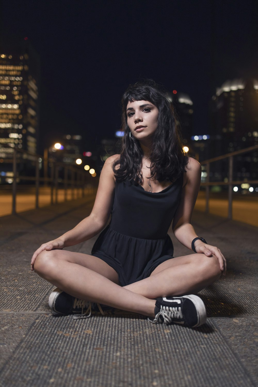 woman in black tank top and black shorts sitting on gray concrete floor during night time