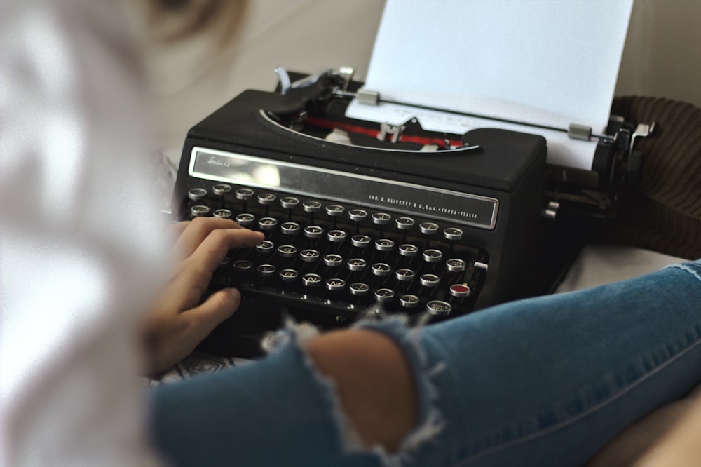 persona in camicia a maniche lunghe blu con macchina da scrivere nera