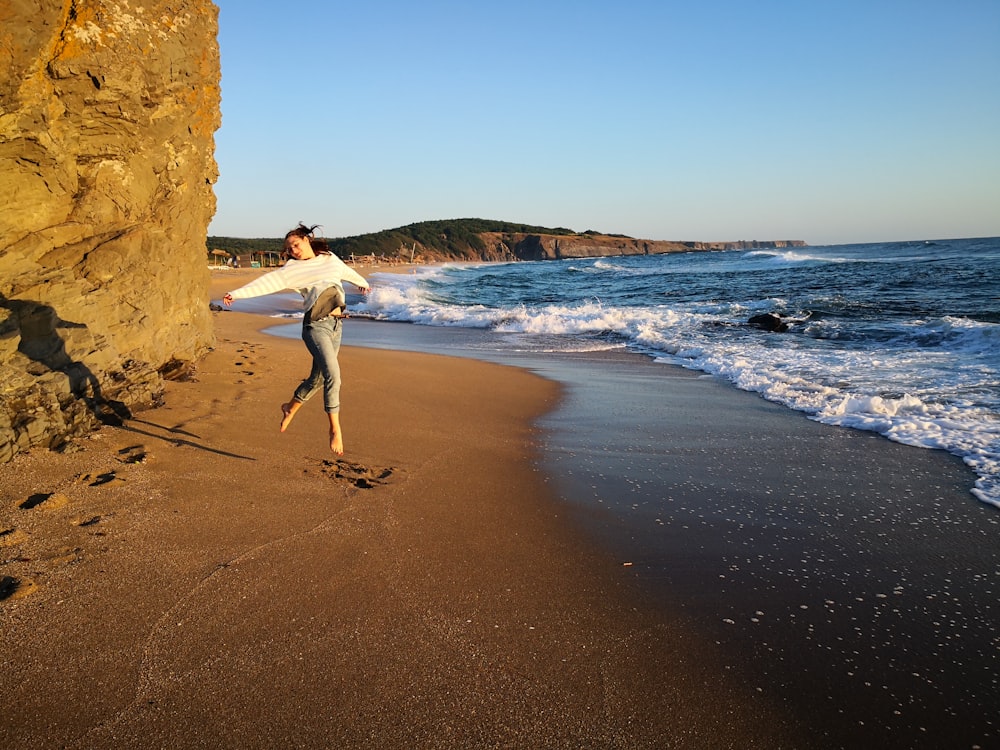 woman in white long sleeve shirt and white pants standing on brown sand beach during daytime