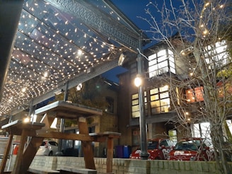 A cozy evening scene under the large wooden gazebo with picnic benches and string lights glowing warmly.