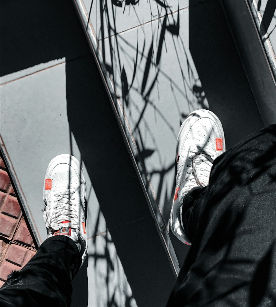 person in black pants and white and red sneakers standing on black and white skateboard during