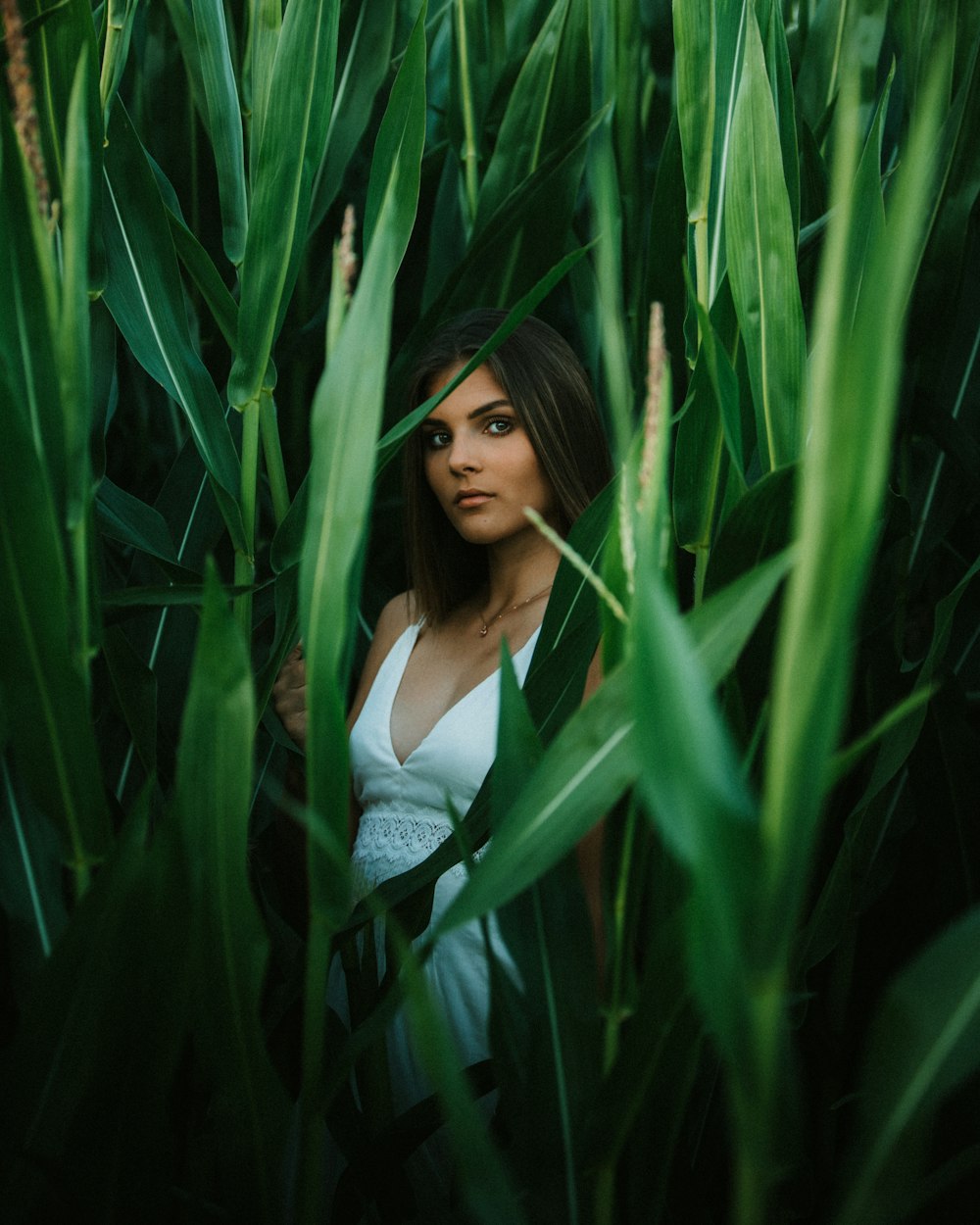 woman in white tank top standing beside green plants during daytime