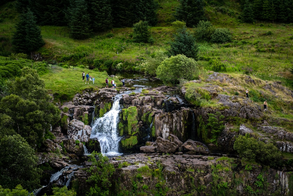 people standing on green grass field near waterfalls during daytime