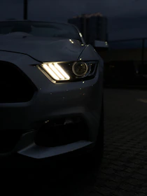 Close-up of a high-end car's headlight glowing against a dark urban background.