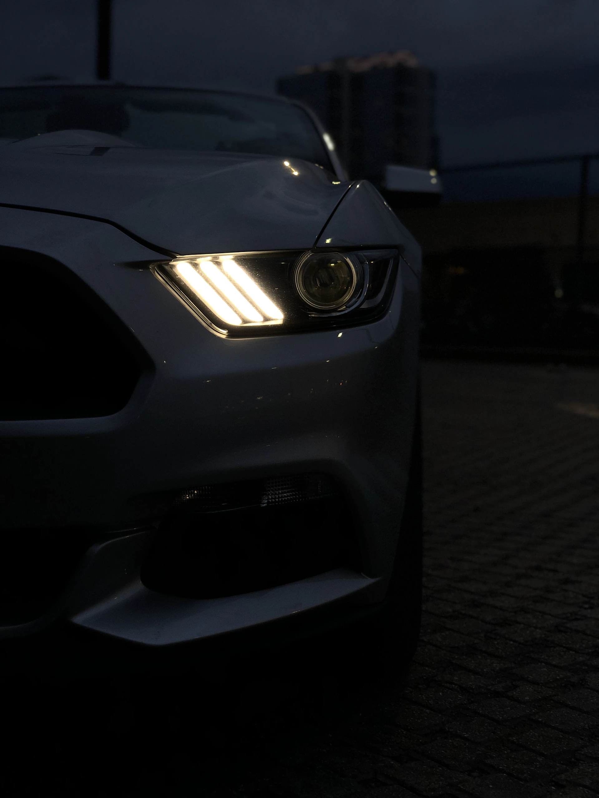 A sleek car outfitted with glowing LED headlights cruising on a city street at dusk, highlighting style and performance.