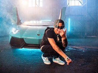 man in black t-shirt and blue denim jeans sitting on car hood