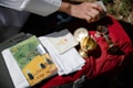 A hand holding a rectangular object over a red bag, which has a collection of religious items resting on it, including a magazine titled 'Magnificat' with a binder clip, white cloths, and several gold-colored chalices and containers.