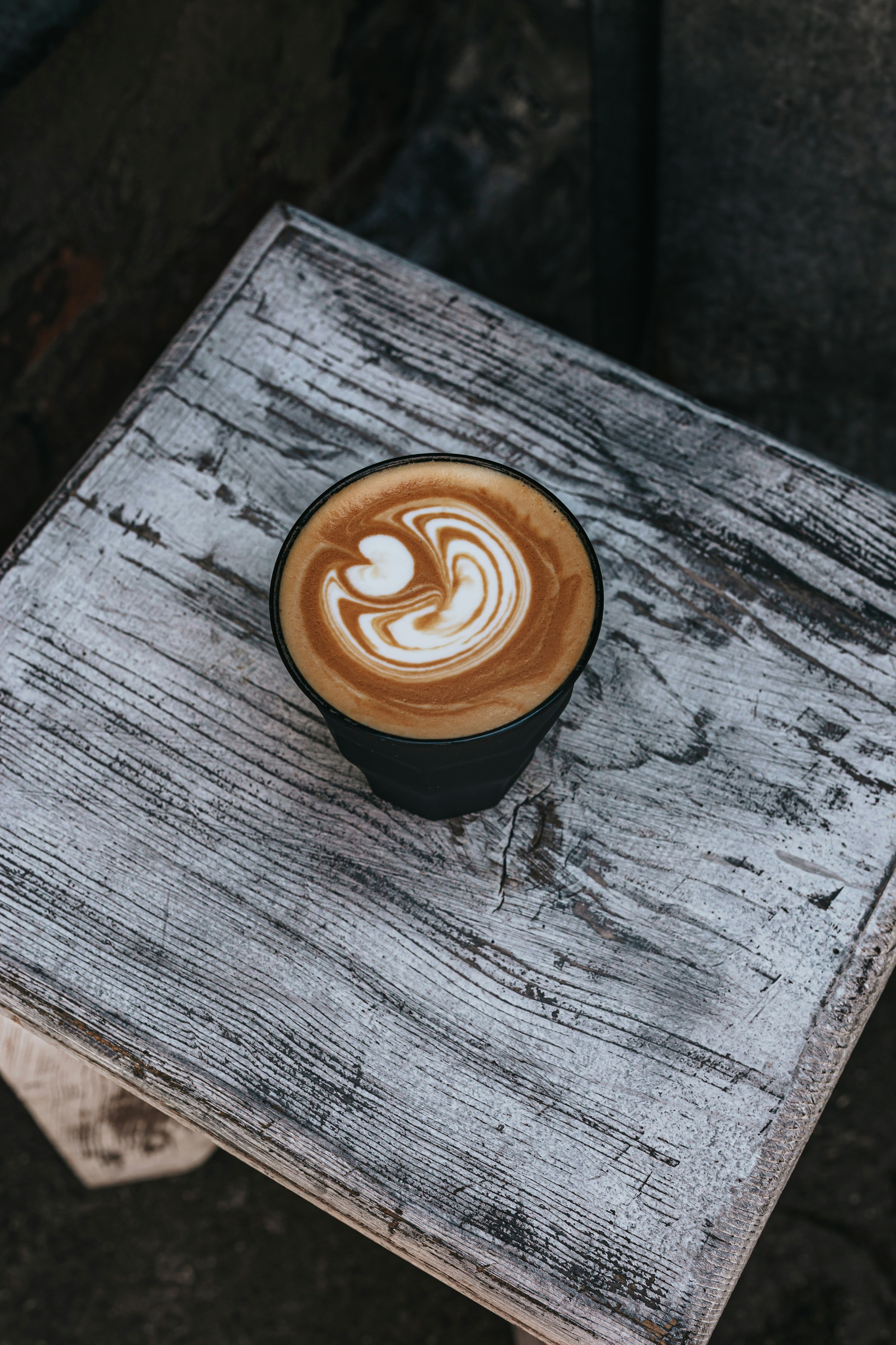 black ceramic cup with brown and white liquid on brown wooden table