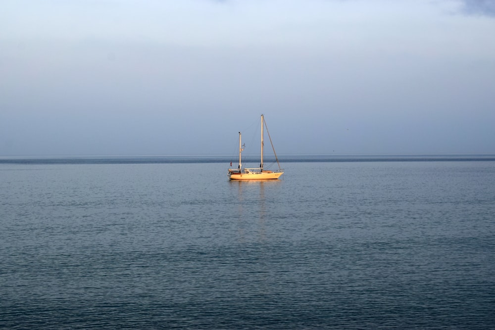 white sail boat on sea under gray sky