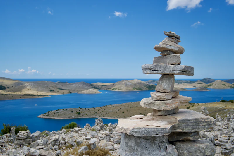 The bare islands of the Kornati in deep blue water, seen past a stone cairn on Žut