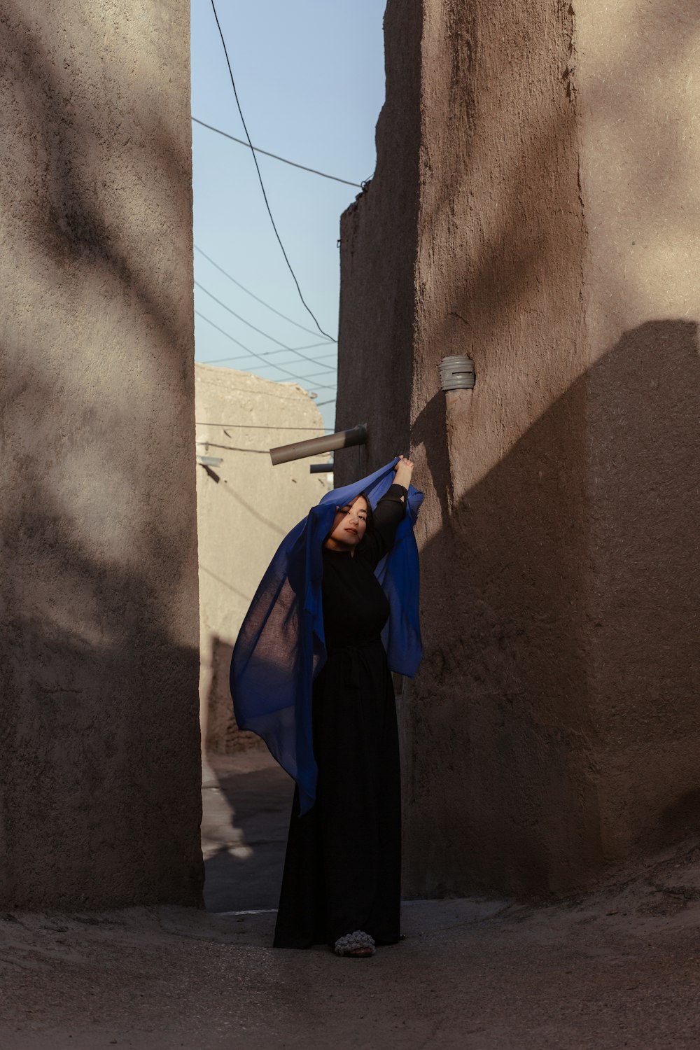 person in blue and black robe standing beside brown concrete wall during daytime