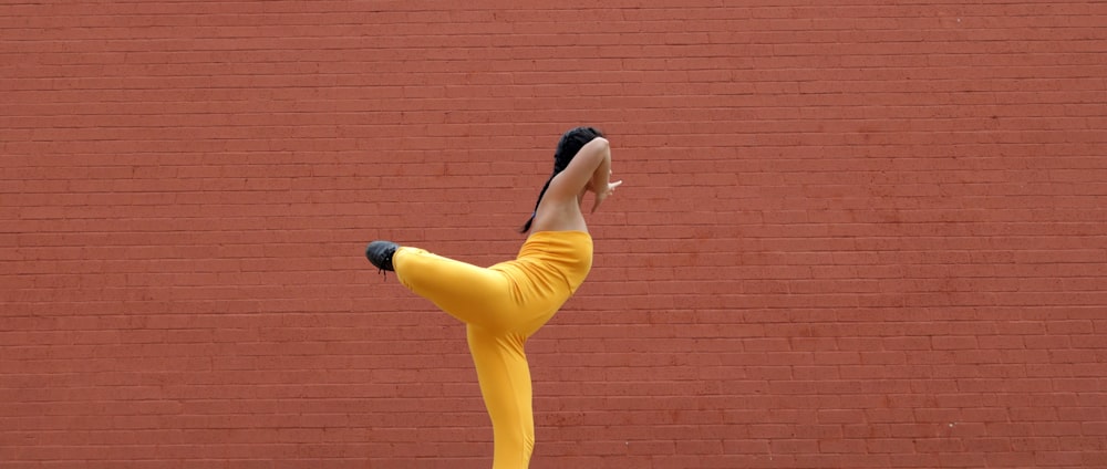 woman in yellow tank top and blue pants standing beside brown brick wall