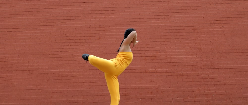 Femme en débardeur jaune et pantalon bleu debout à côté d’un mur de briques brunes