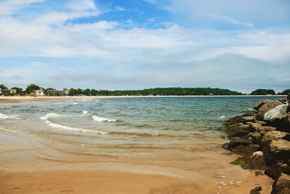 body of water near green trees under white clouds and blue sky during daytime