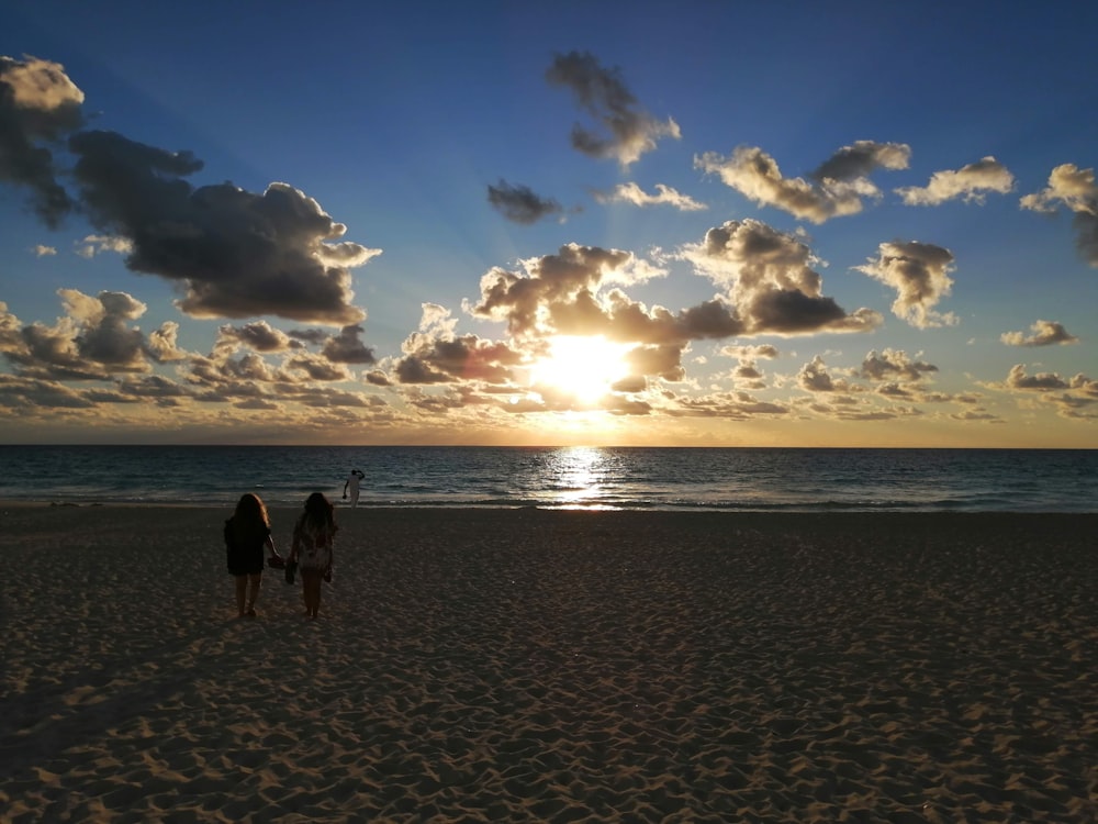 2 people walking on beach during sunset