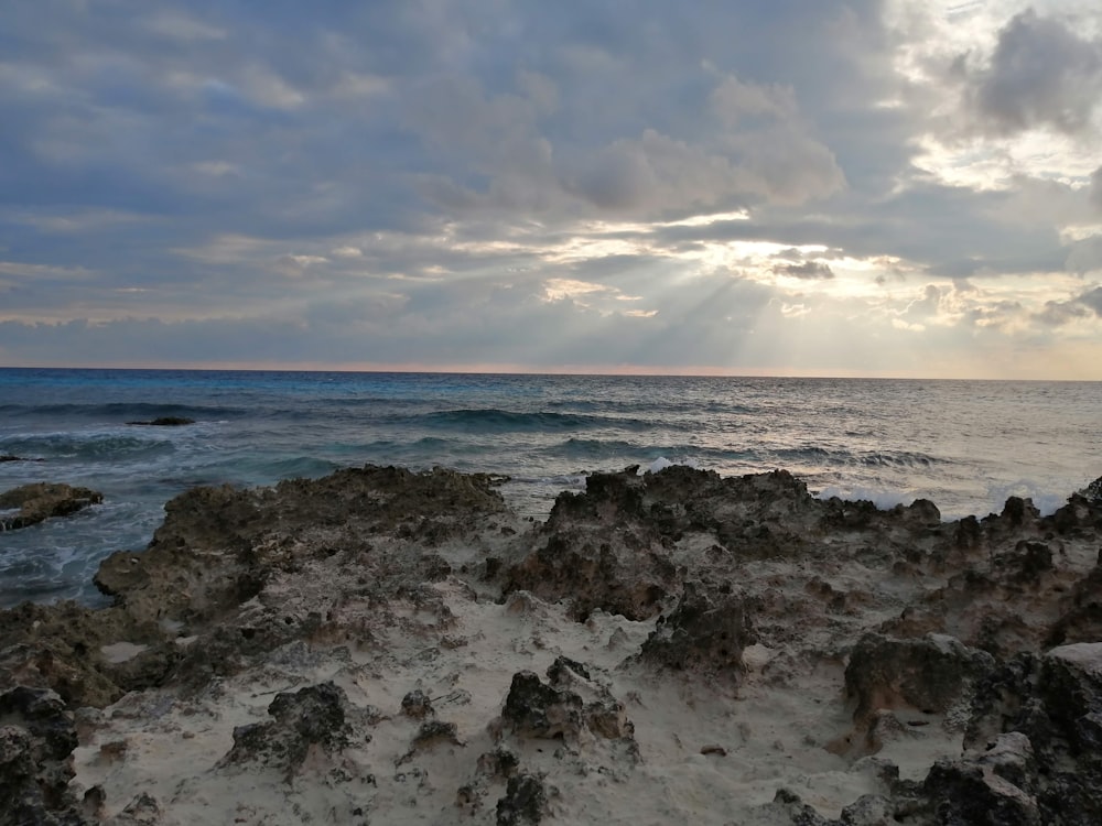 Onde dell'oceano che si infrangono sulle rocce sotto nuvole bianche e cielo blu durante il giorno