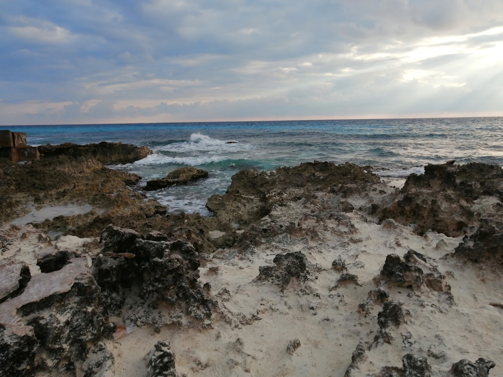 Rocce marroni in riva al mare sotto nuvole bianche e cielo blu durante il giorno