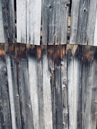 Weathered wooden planks aligned vertically, showing natural grain patterns and variations in color due to exposure and aging.