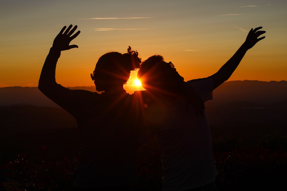 silhouette of man and woman raising hands during sunset