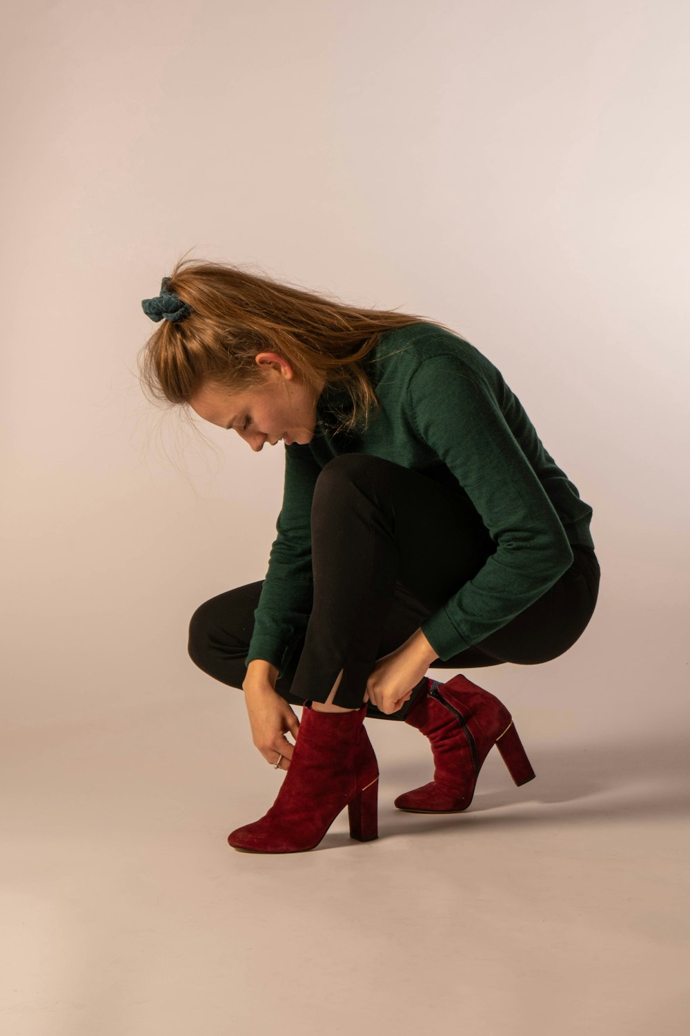 Femme en chemise verte à manches longues et bottes rouges assise sur un sol blanc