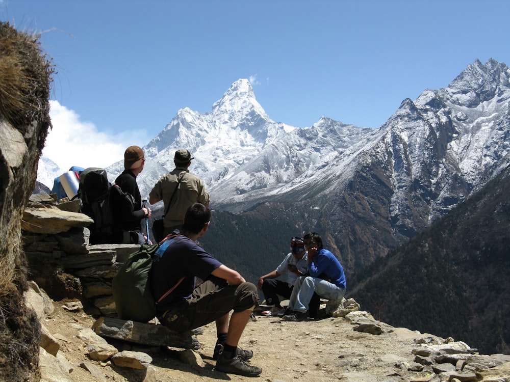 people sitting on rock near snow covered mountain during daytime