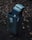 An old, rusted electronic device, possibly a cash register or electronic machine, is discarded inside a public trash bin. The bin is situated outdoors among dry leaves and twigs. Graffiti and stickers are visible on the bin’s surface, adding urban elements to the scene.
