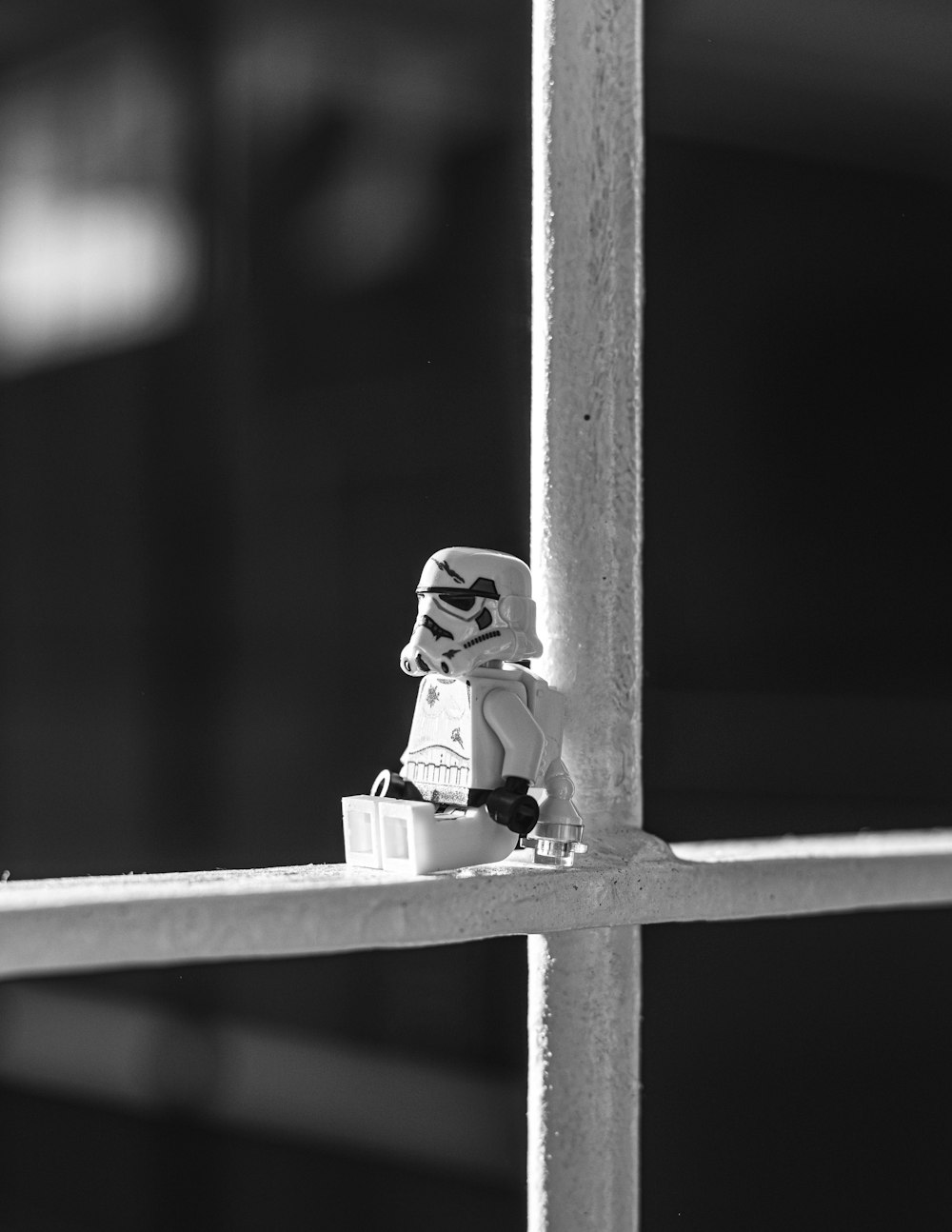 grayscale photo of lego mini figure on wooden fence