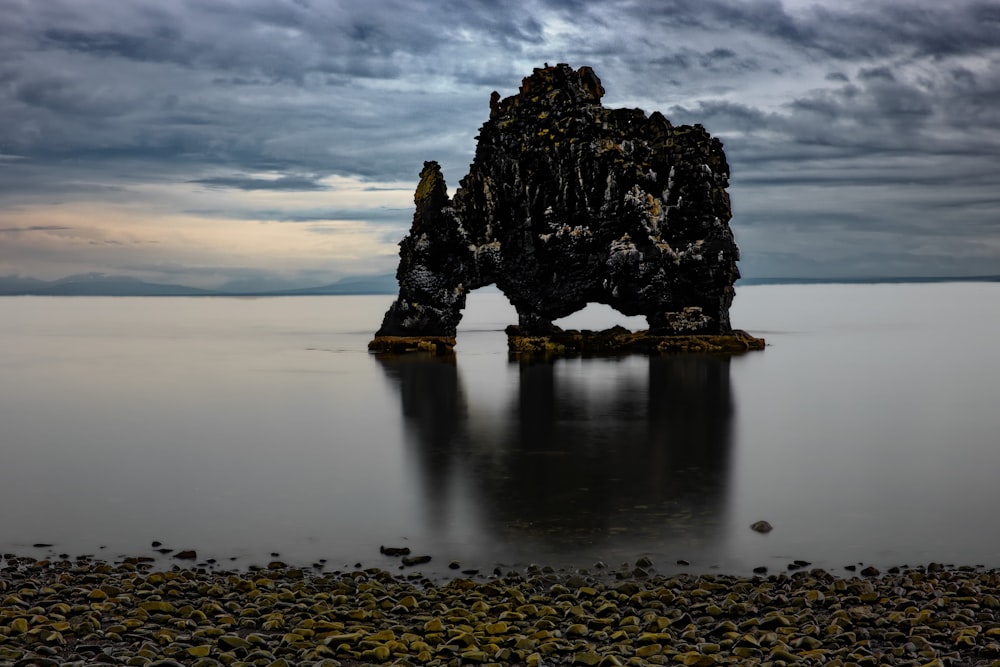 rock formation on body of water under cloudy sky during daytime