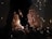 A worker uses a grinder on metal, creating bright sparks that illuminate the dimly lit environment.
