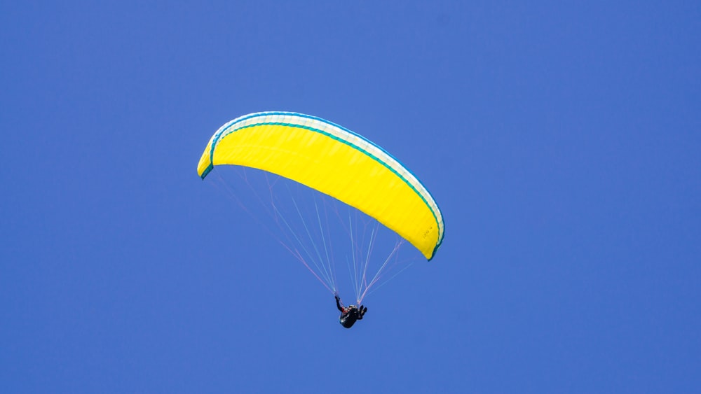 낮 동안 푸른 하늘 아래 노란 낙하산을 탄 사람