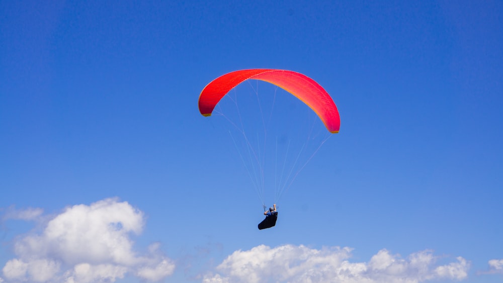 persona in paracadute rosso sotto cielo blu durante il giorno