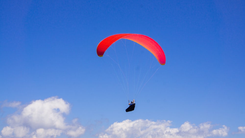 person in red parachute under blue sky during daytime