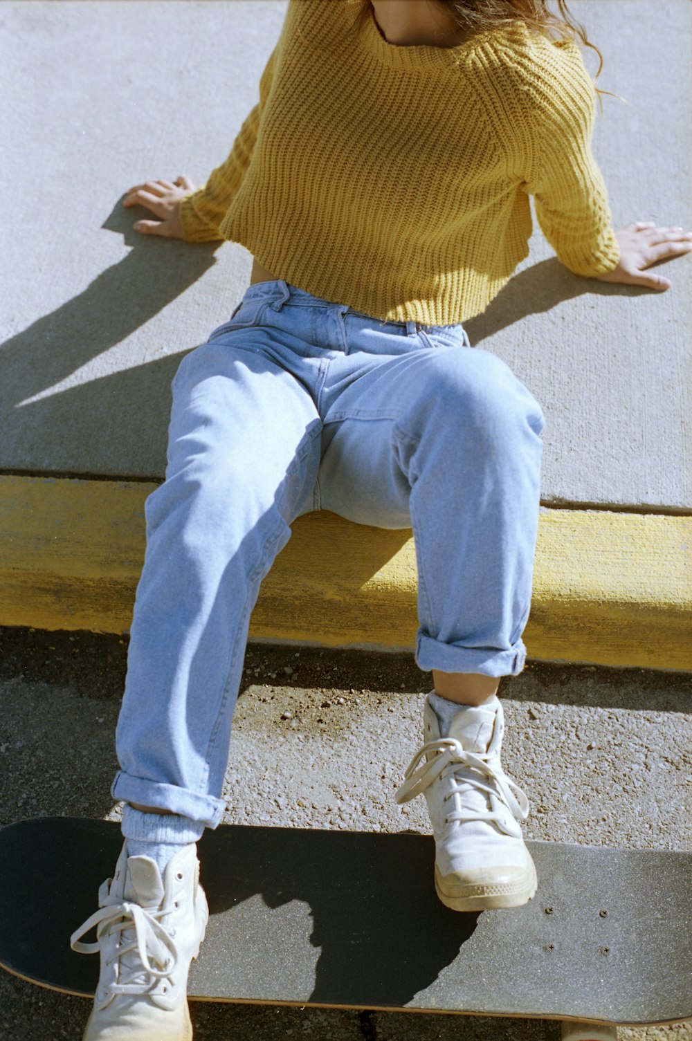 person in yellow sweater and gray denim jeans sitting on brown wooden bench