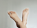 Two crossed feet positioned against a plain light-colored background, displaying clean and well-maintained toenails.