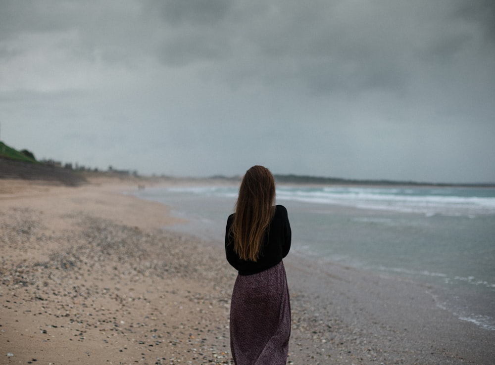 a woman standing on a beach looking at the ocean