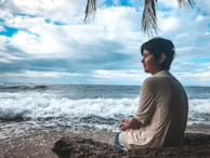 Traveler meditating on a rocky shore surrounded by lush tropical plants.