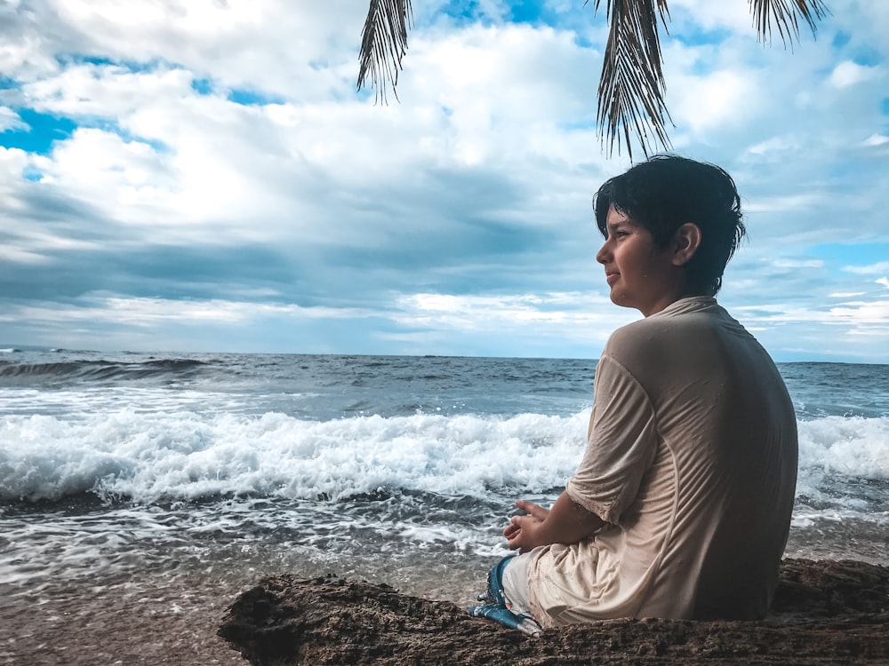 man in brown long sleeve shirt sitting on brown rock near sea during daytime