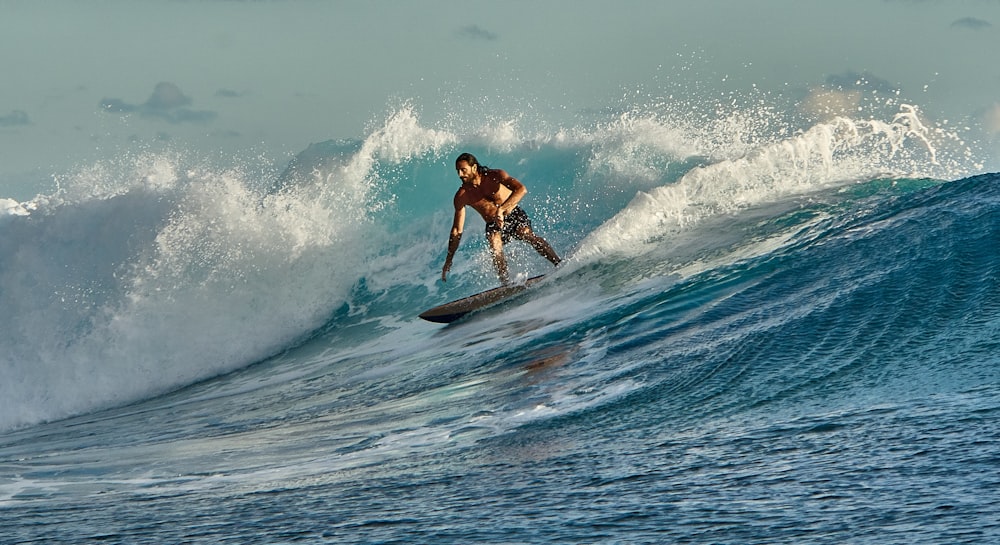 uomo in pantaloncini neri che fa surf sulle onde del mare durante il giorno