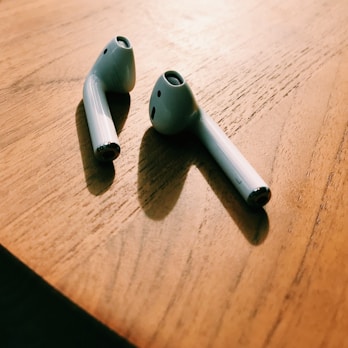 A pair of wireless ear pods resting on a wooden table with soft natural light.