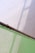 A metal pipe extends diagonally across the image, casting shadows on a light-colored wall. Below, a semi-transparent green sheet, possibly a tarp or covering, is draped and secured with metal grommets.
