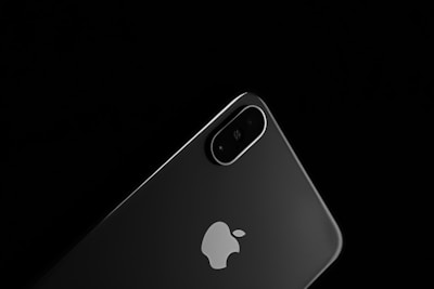 A sleek, modern smartphone with a dual camera setup on the back. The device is black with a reflective glass finish and features a prominent brand logo in the center. The background is dark, emphasizing the phone's minimalist design and glossy surface.