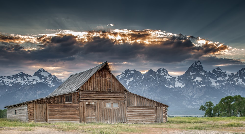 brown wooden barn near snow covered mountain under cloudy sky during daytime