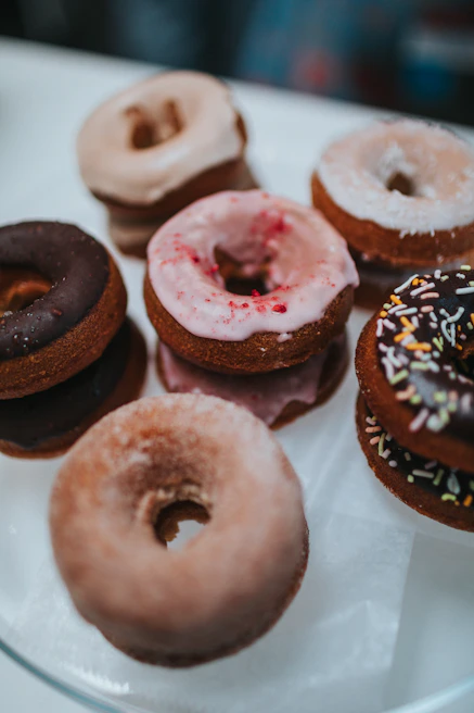 An assortment of vegan donuts with various glazes and toppings arranged on a ceramic plate