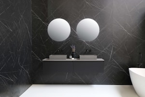 A modern bathroom features two round mirrors mounted on a dark textured wall with a marble pattern. Below the mirrors, there are two rectangular sinks with a minimalist design, accompanied by matching dark faucet fixtures. A vase with decorative items and a small container are placed on the countertop. To the right, a sleek white bathtub adds contrast to the ambiance.