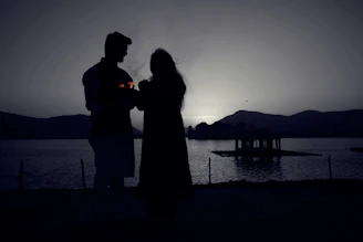 A softly lit photo of a couple holding hands by the shore of Lake Como at sunset.