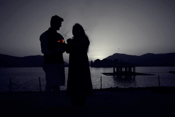 A softly lit photo of a couple holding hands by the shore of Lake Como at sunset.
