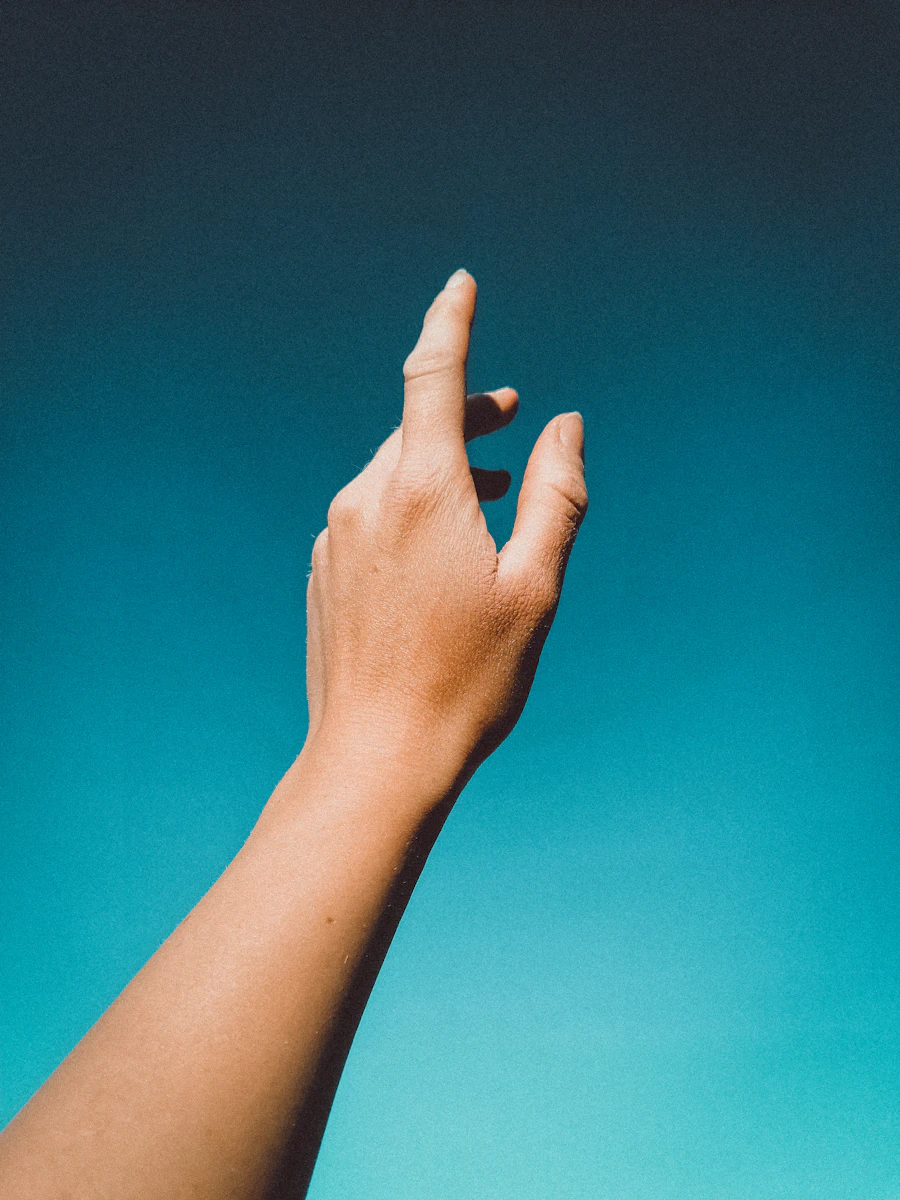 A hand reaching upward against a clear sky