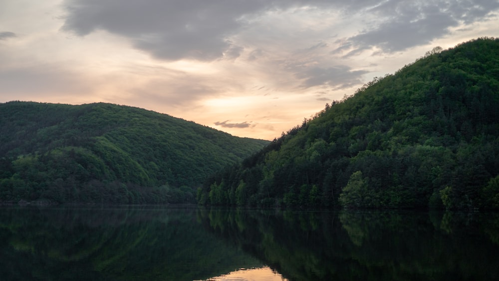 green mountains beside lake under cloudy sky during daytime