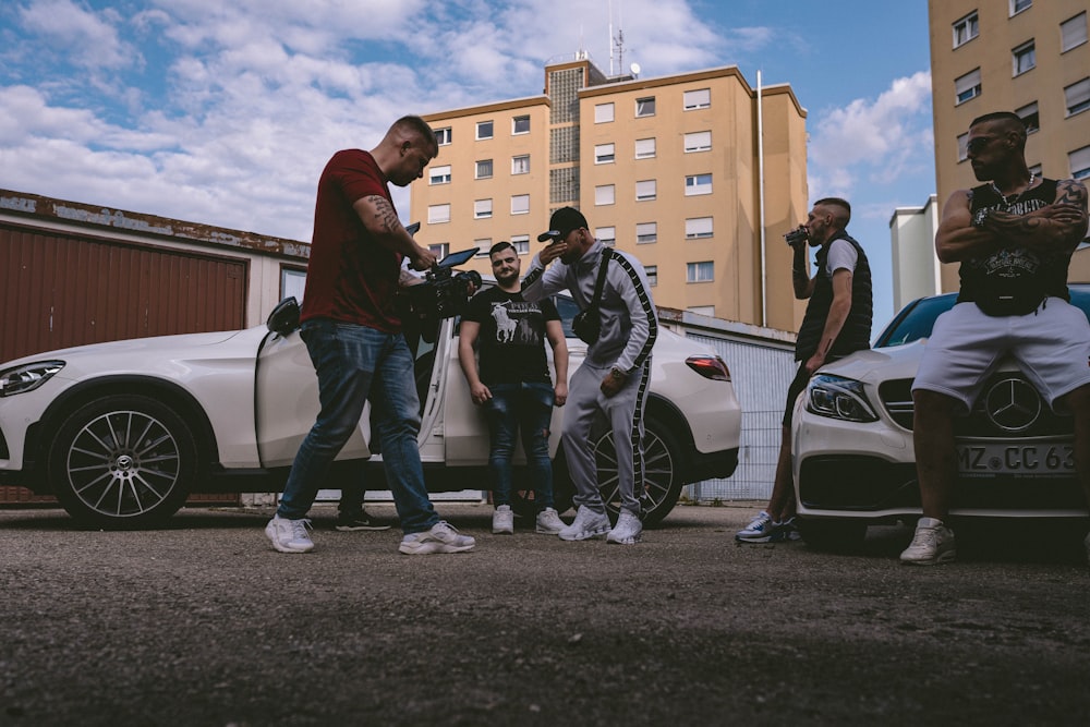 man in black t-shirt and blue denim jeans standing beside white car during daytime